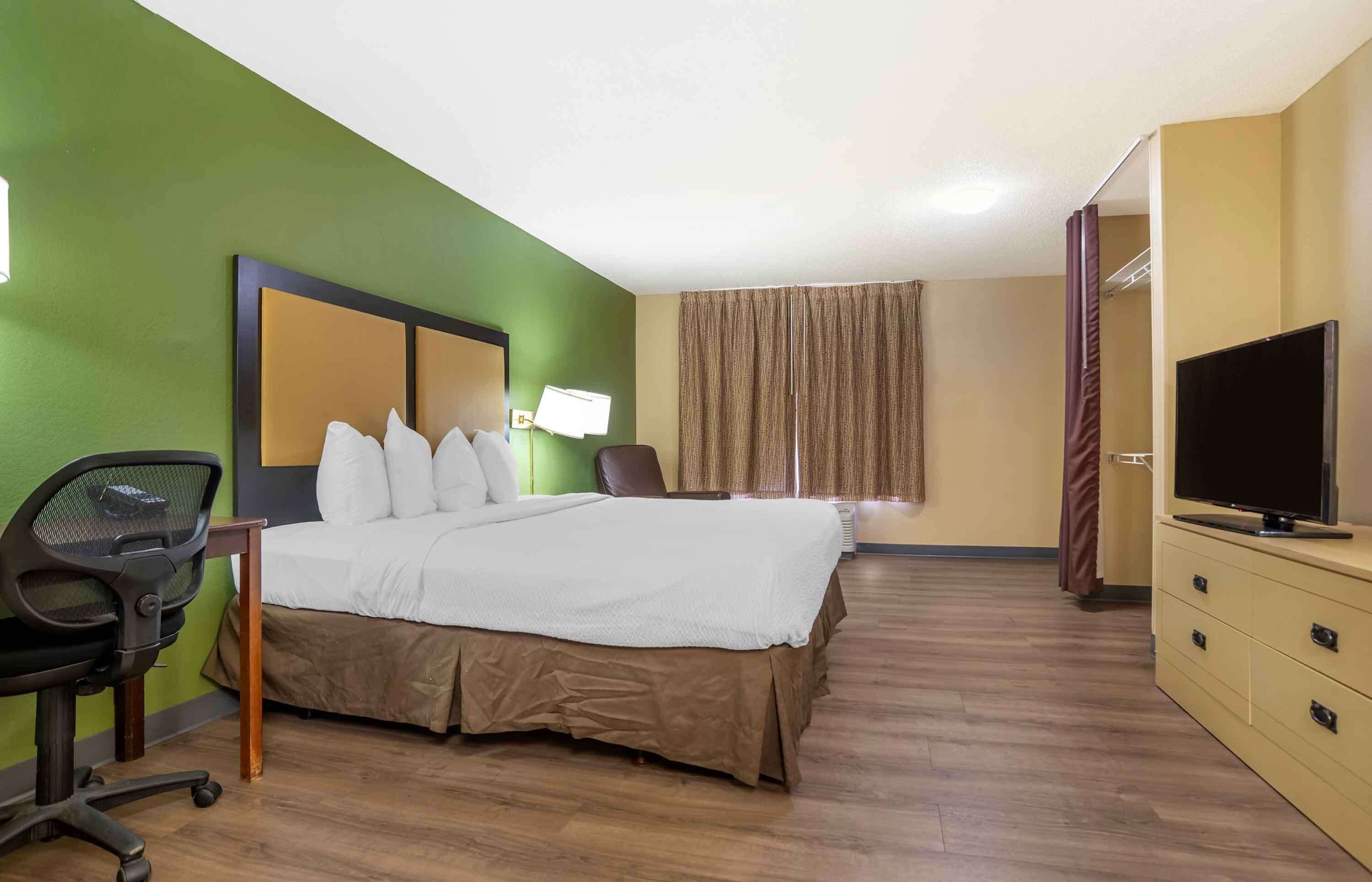 A hotel room with a bed, a desk, a chair, a television, and a wardrobe.