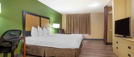 A hotel room with a bed, a desk, a chair, a television, and a wardrobe.