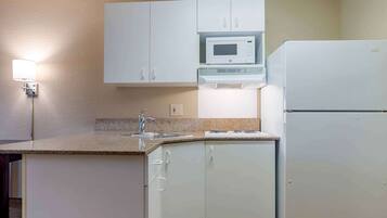 A compact kitchen with white cabinets, a microwave, a refrigerator, a sink, and a countertop.