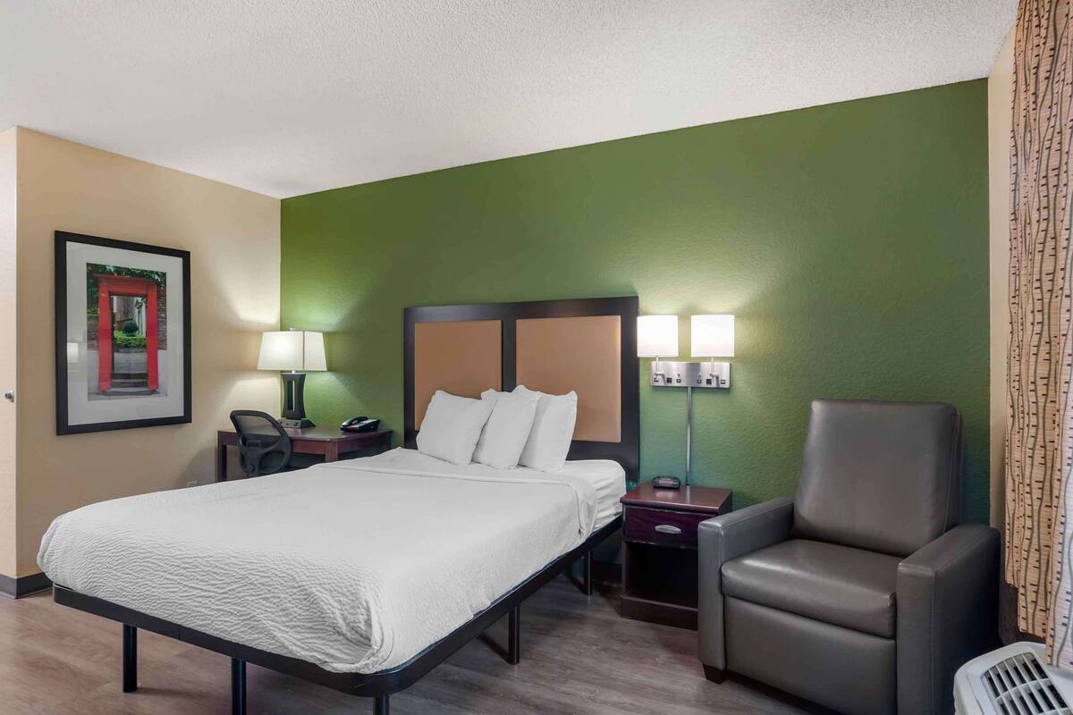 Une chambre d’hôtel avec un lit, une chaise, un bureau et une table de chevet.