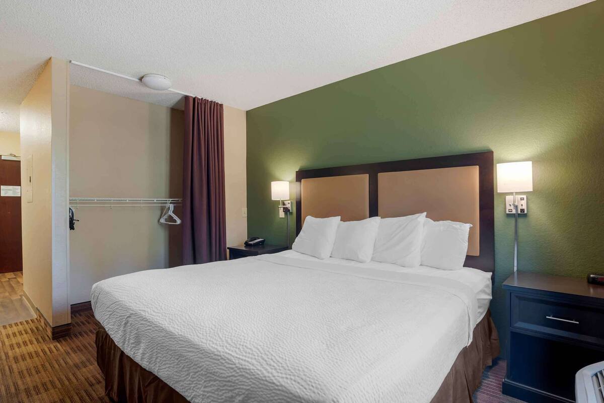 Une chambre d’hôtel avec un grand lit, deux tables de chevet avec des lampes, une armoire et une salle de bain avec un rideau de douche.