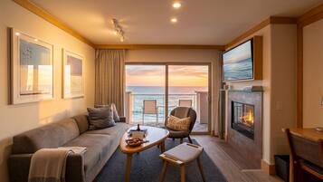 A modern living room with a sofa, a small table, a chair, a fireplace, and a large window with a view of the ocean.