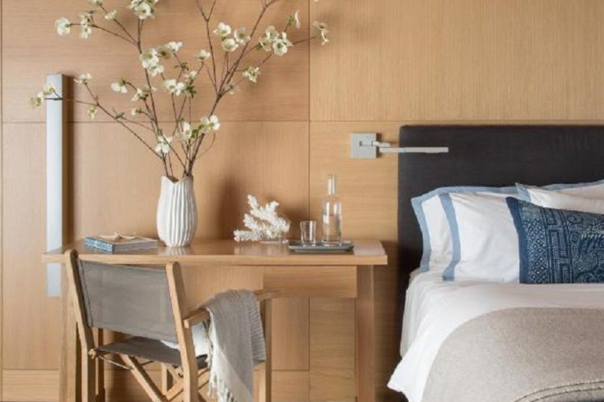 Une chambre à coucher avec une tête de lit en bois, une table de chevet ornée d’un vase de fleurs, une chaise et un lit avec des oreillers.