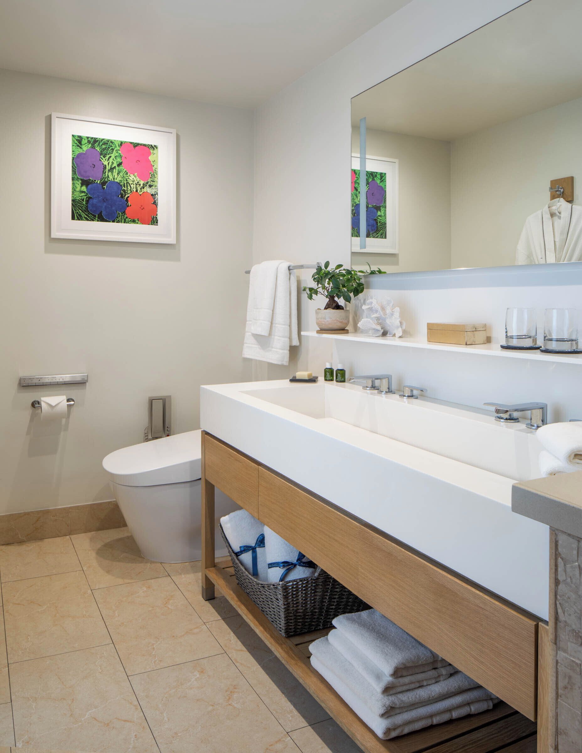 A modern bathroom with a white sink, a toilet, a mirror, and a framed artwork on the wall.
