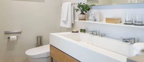 A modern bathroom with a white sink, a toilet, a mirror, and a framed artwork on the wall.