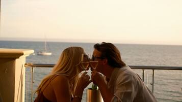 A couple sitting at a table with a view of the sea and a sailboat in the distance.