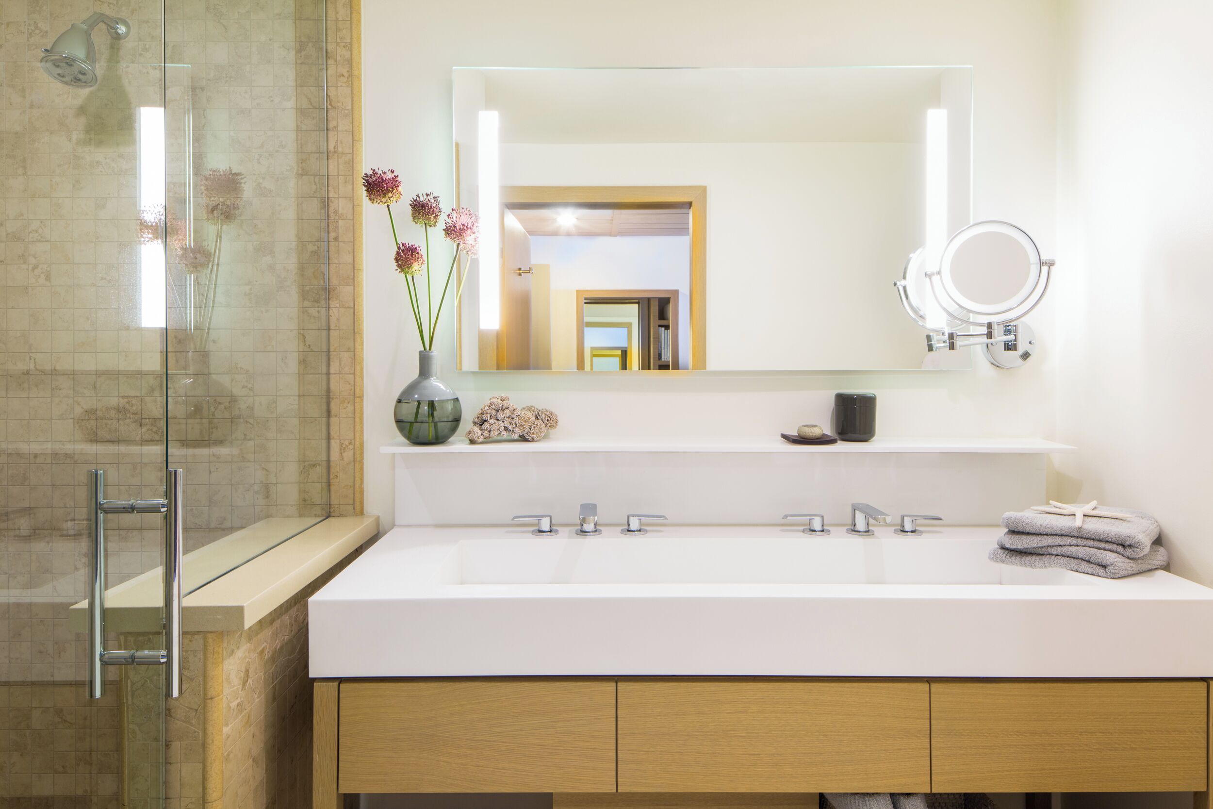 A modern bathroom with a glass shower enclosure, a white sink with a mirror above it, and wooden cabinets below.