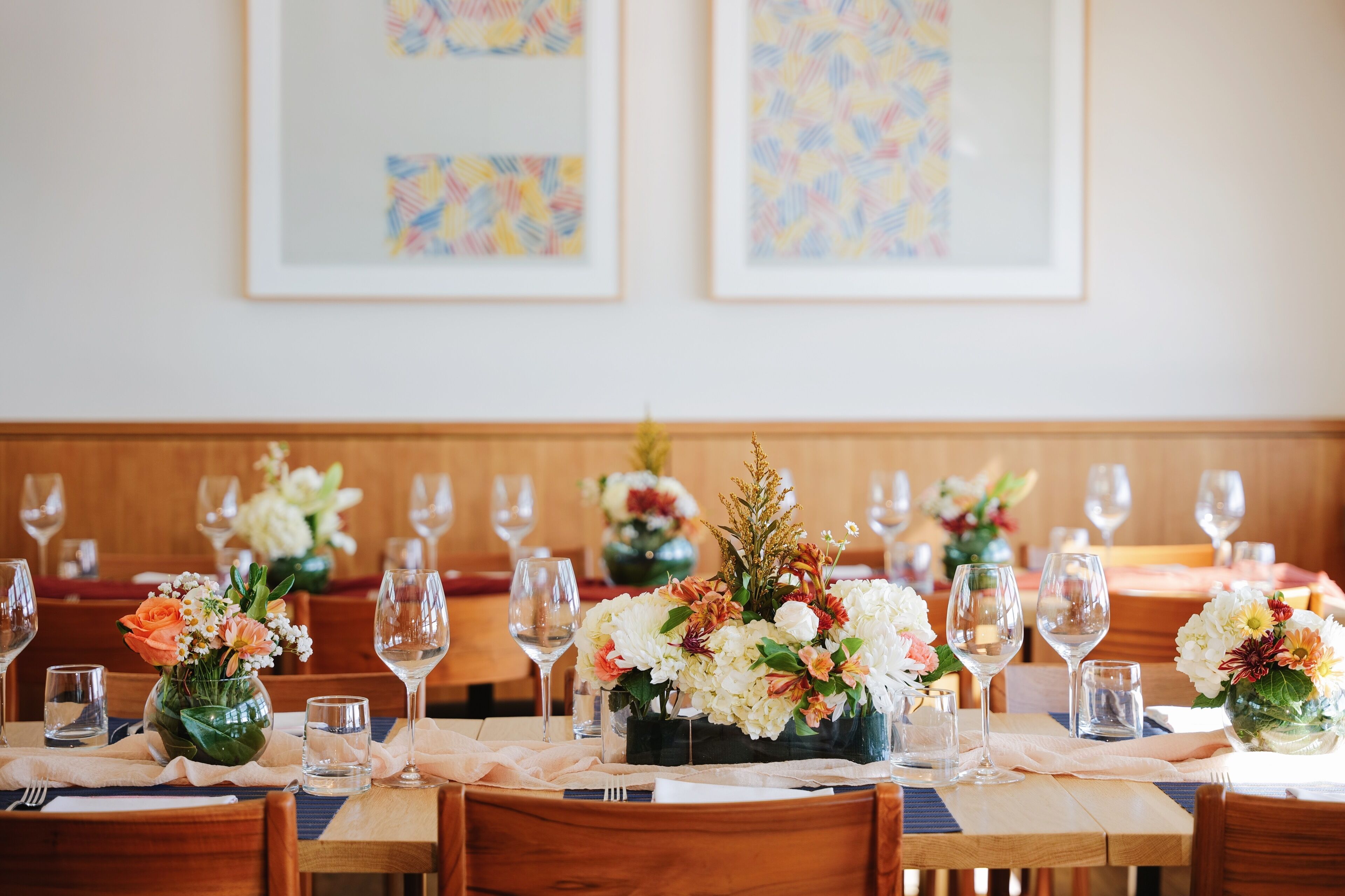 A dining area with tables set for a meal, each with a vase of flowers and wine glasses.