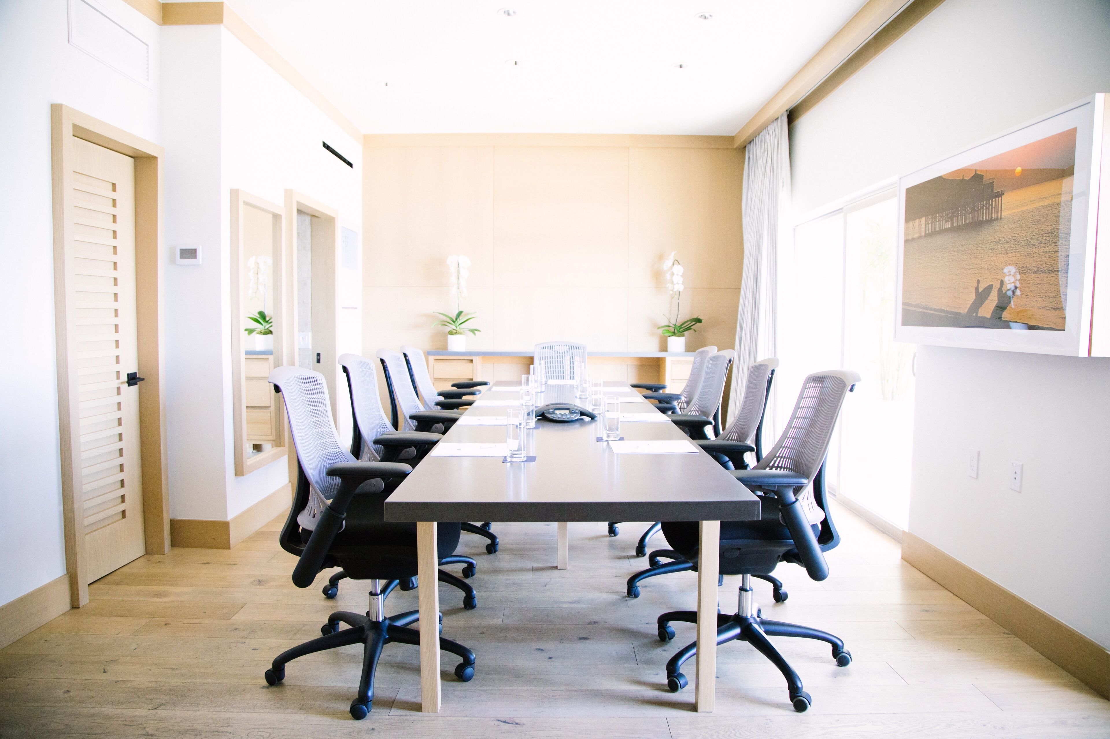 A conference room with a long table, multiple chairs, and potted plants.