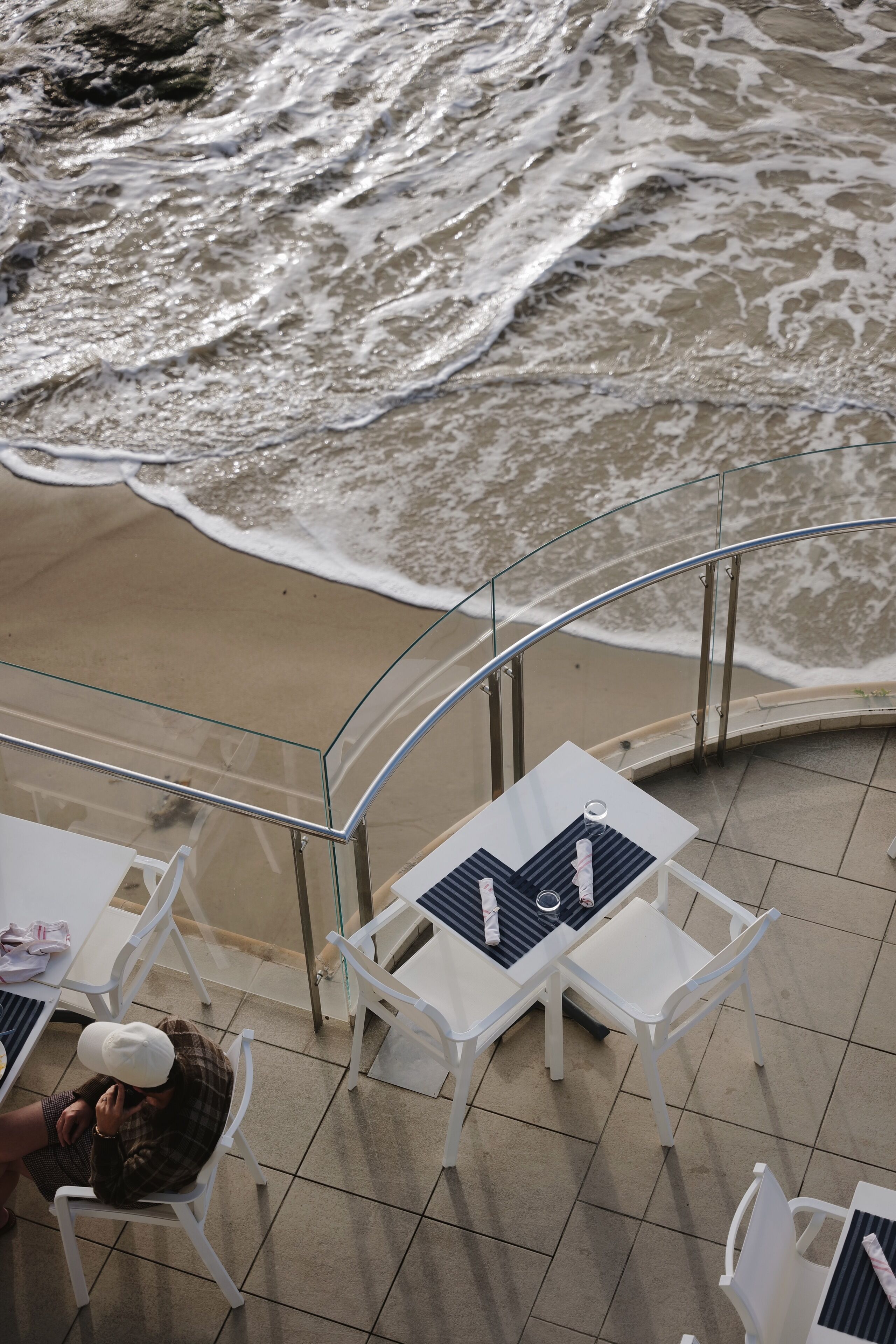 Una terraza frente a la playa con sillas y mesas blancas, con vistas al océano.