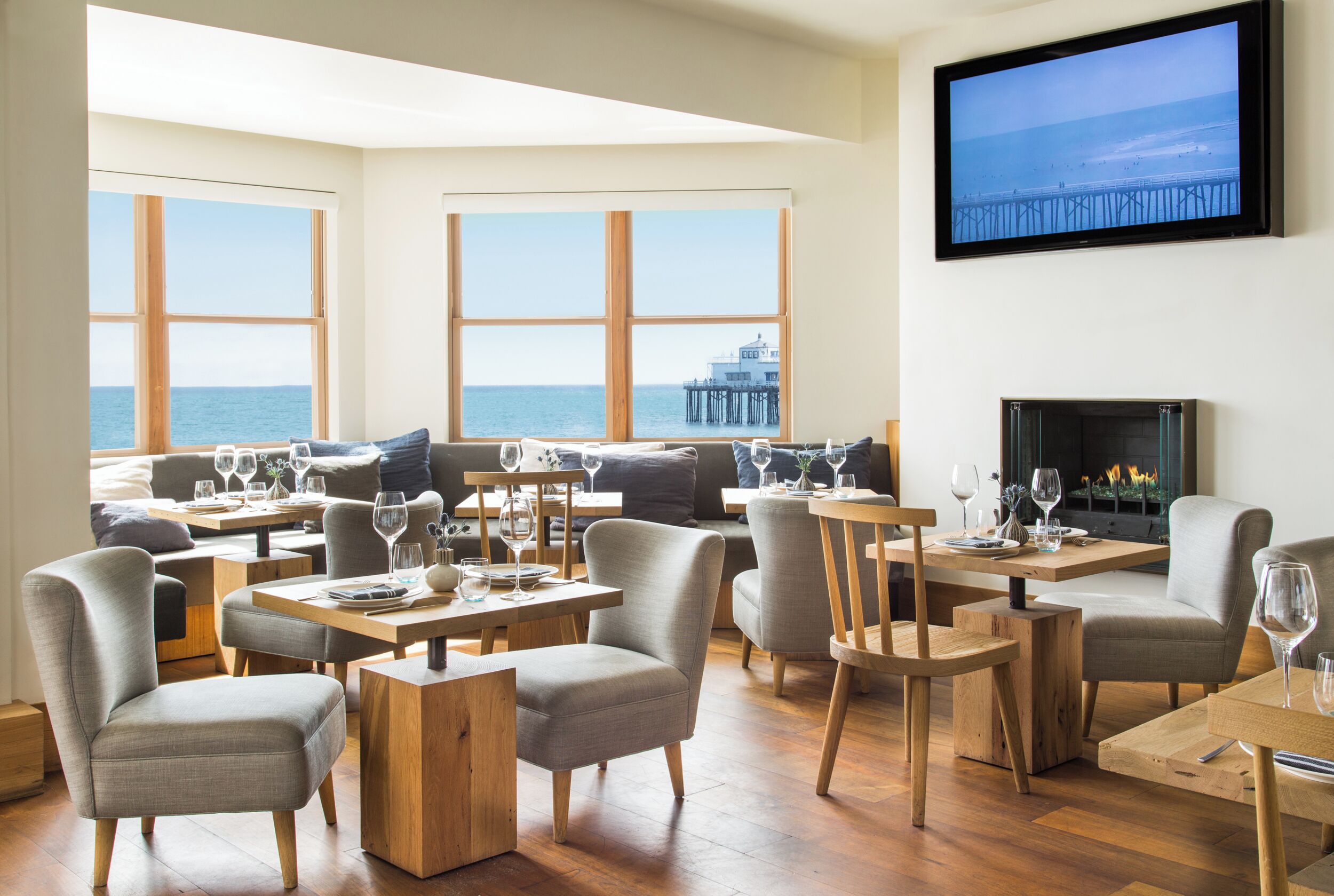 A dining area with tables and chairs, a fireplace, and large windows overlooking the sea.