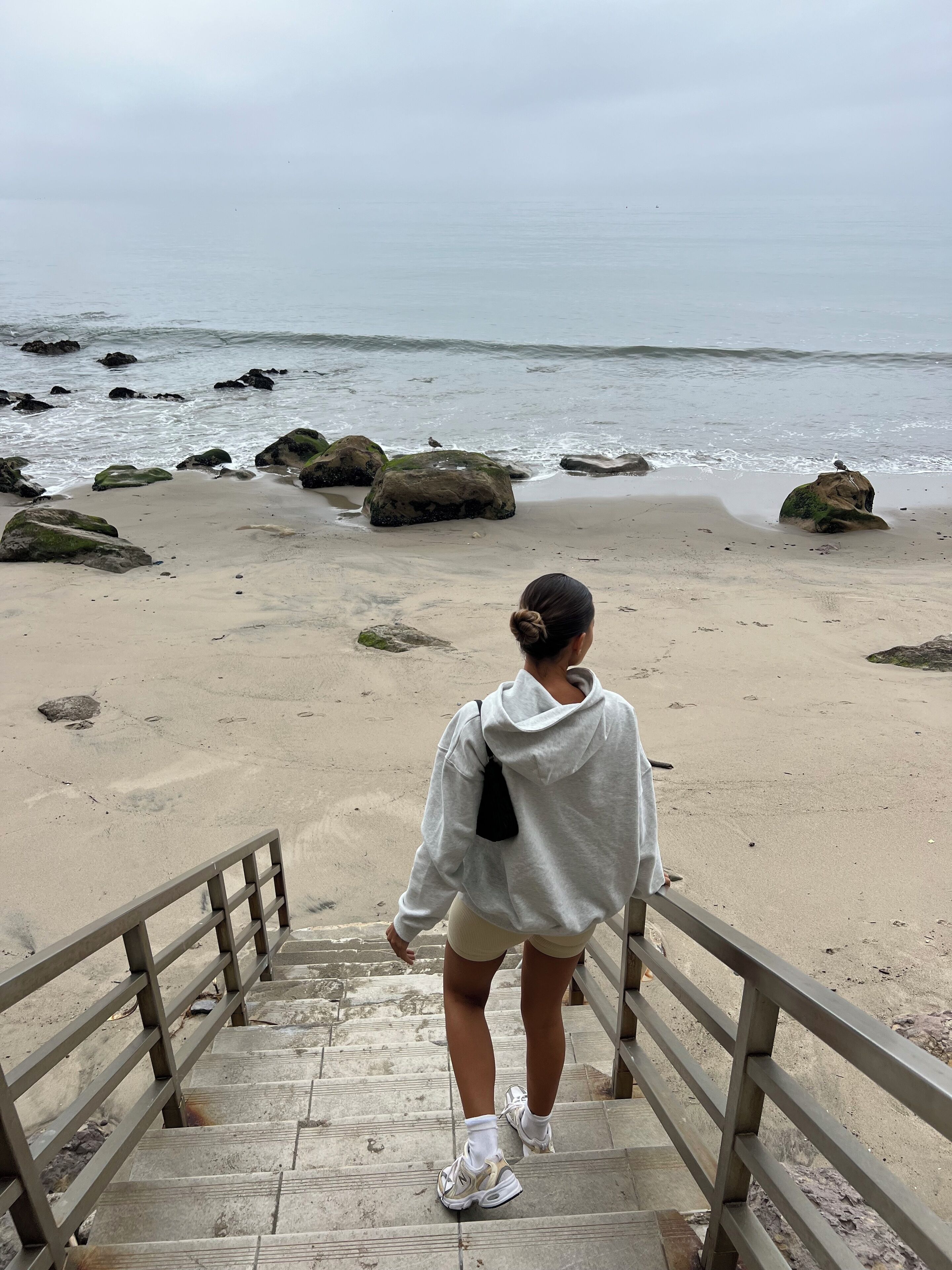 Egy személy egy lépcsőn lefelé halad egy olyan strand felé, ahol sziklák és a tenger látható a háttérben.