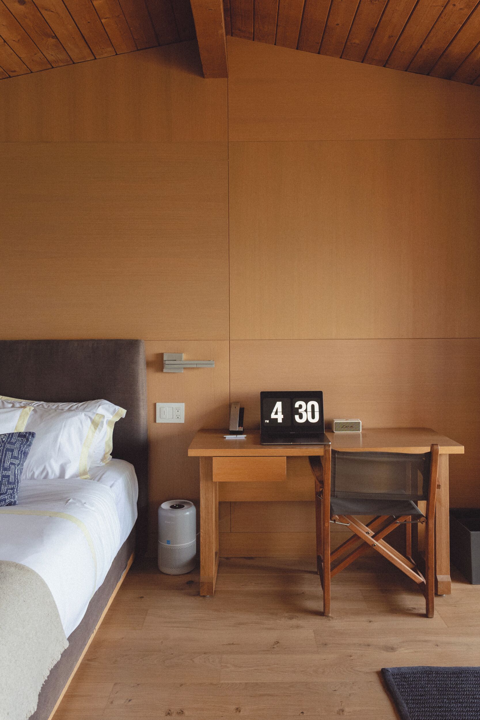 Een slaapkamer met een bed, een bureau, een laptop en een klok waarop 4:30 uur staat.