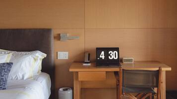 Een slaapkamer met een bed, een bureau, een laptop en een klok waarop 4:30 uur staat.