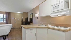 Quarto de hotel pequeno com cozinha compacta, cama, televisão e banheiro.