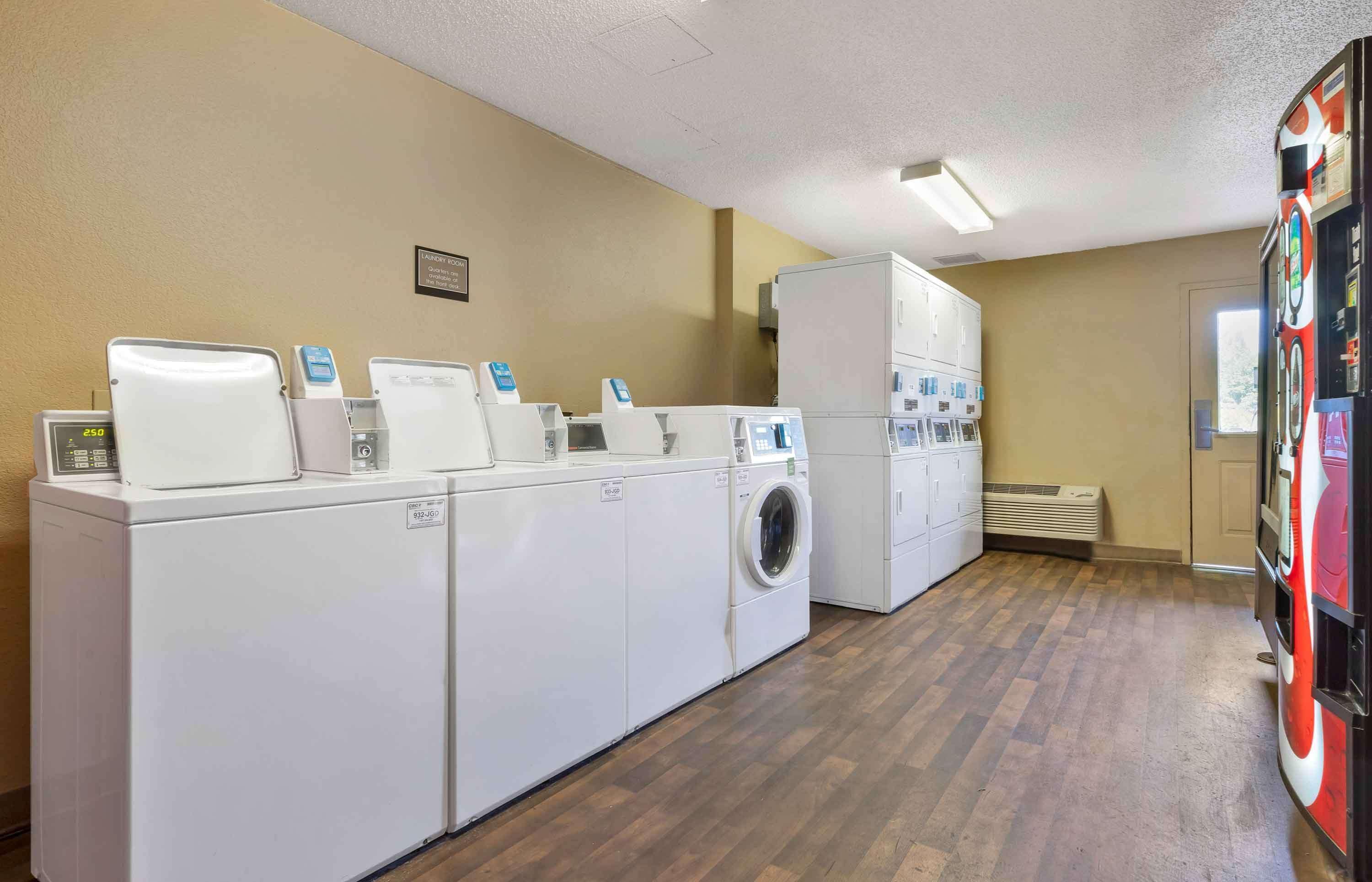 Een wasserette met meerdere wasmachines en drogers, een ventilatiesysteem en een automaat.