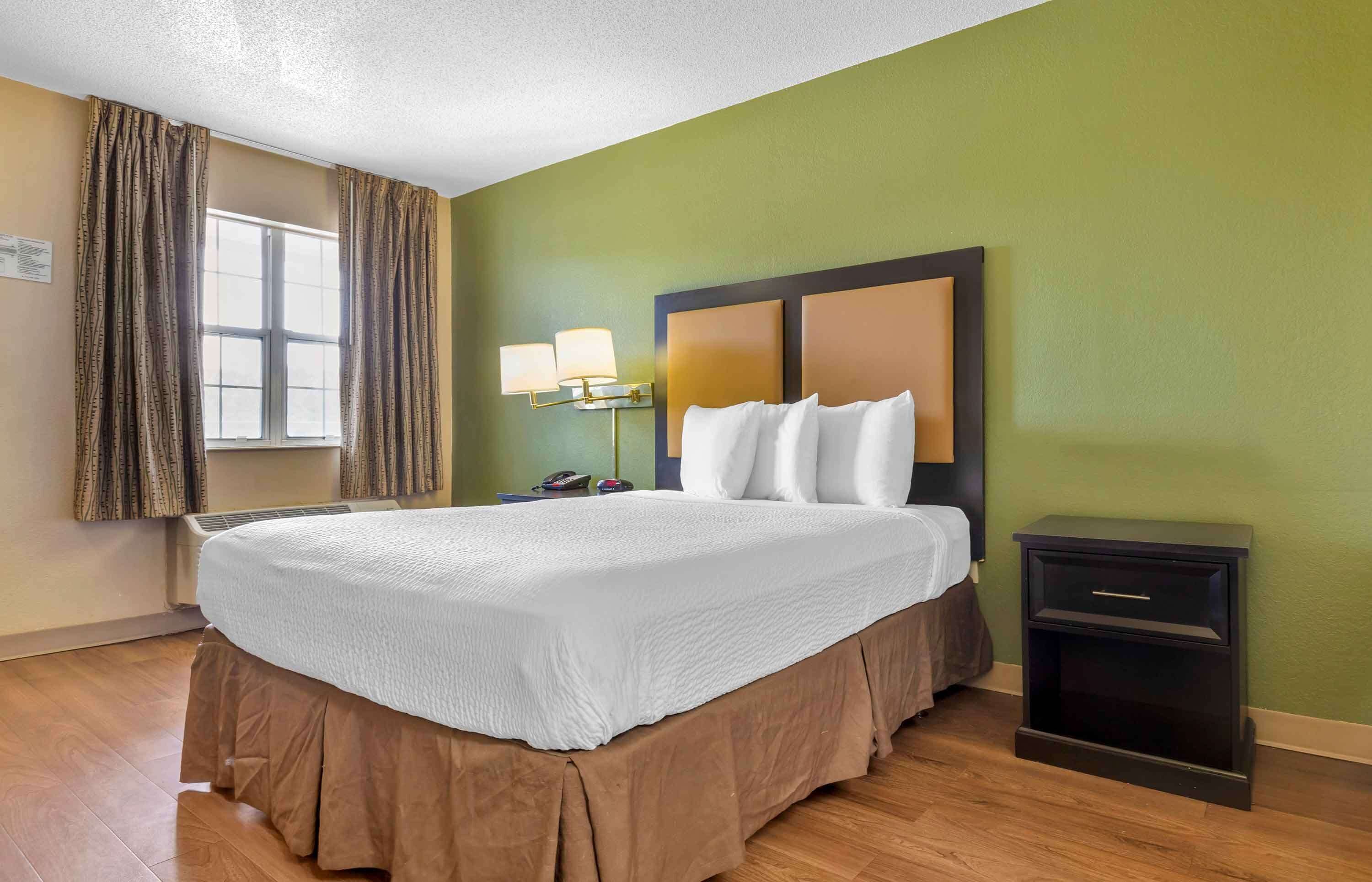 Een hotelkamer met een groot bed, een nachtkastje, een lamp en een raam met gordijnen.
