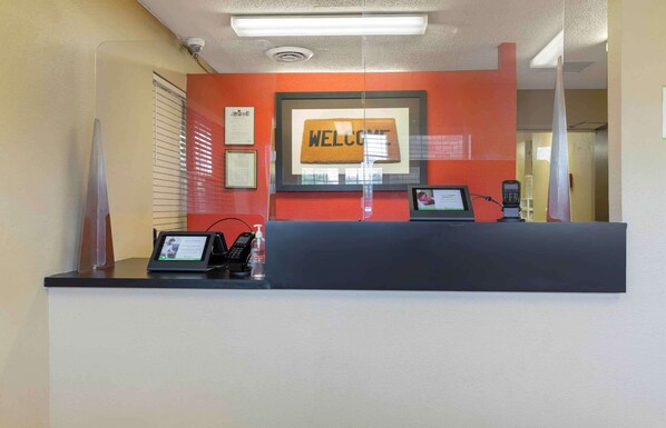Een receptiebalie met een 'WELCOME' bord, een telefoon, een digitaal scherm en een fles handdesinfectiemiddel.