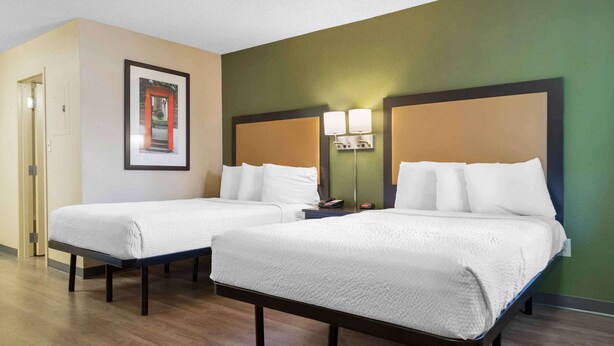 Quarto de hotel com duas camas, um quadro na parede e uma mesa de cabeceira com luminárias.