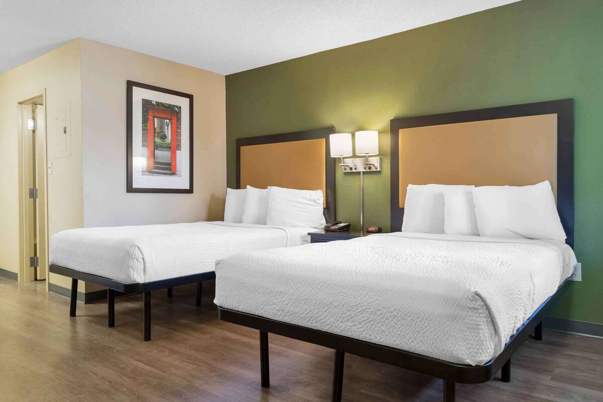 A hotel room with two beds, a framed picture on the wall, and a nightstand with lamps.