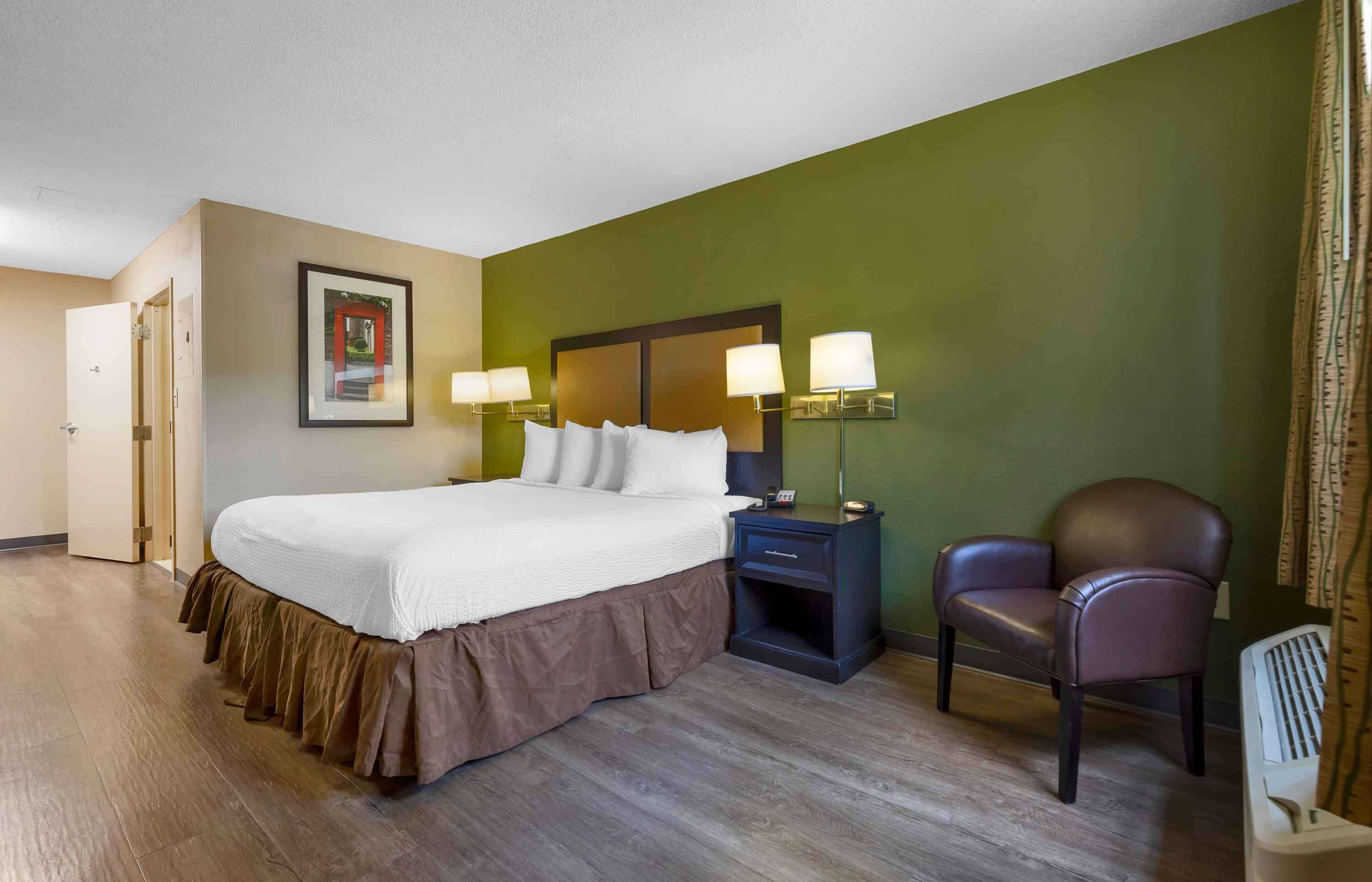 A hotel room with a bed, bedside lamps, a chair, and a desk.