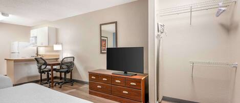 A hotel room with a bed, a desk with a computer, a TV on a dresser, and a shower area.