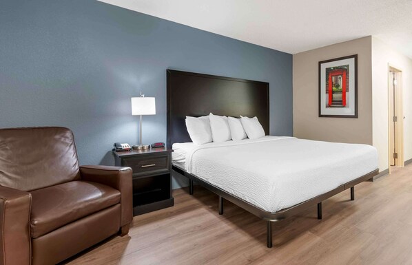 A hotel room with a bed, a brown leather chair, a bedside table with a lamp, and a framed picture on the wall.