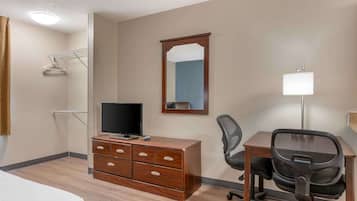 A hotel room with a wooden dresser, a desk with a chair, a flat-screen TV, a mirror, and a lamp.