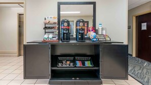 A reception area with a coffee station featuring two coffee makers, a water dispenser, and a bottle of water. There are baskets of snacks and a small refrigerator below the counter. - Extended Stay America Suites Fort Wayne South (Fort Wayne)