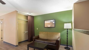 A hotel room with a brown leather sofa, a small table, a floor lamp, and a green accent wall. - Extended Stay America Select Suites Springfield South (Springfield)