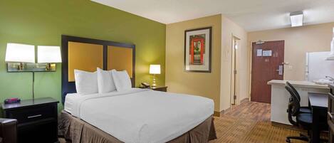 A hotel room with a large bed, bedside lamps, a desk with a chair, and a door with a red frame.