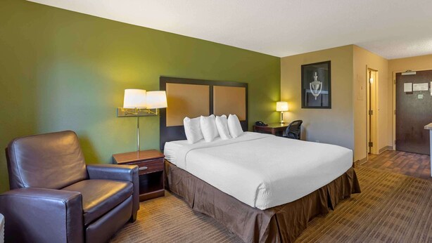 A hotel room with a large bed, a chair, a nightstand, a lamp, and a door. - Extended Stay America Select Suites Springfield South (Springfield)