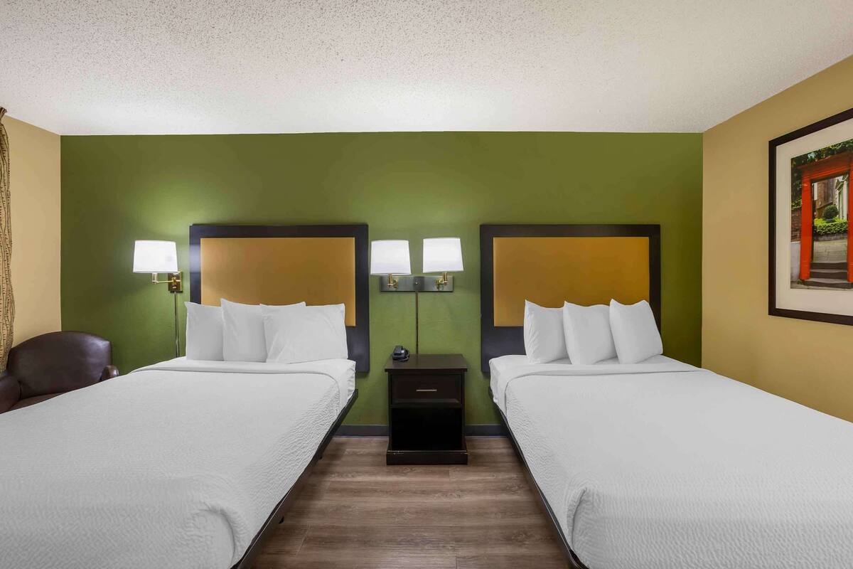 Una habitación de hotel con dos camas, una mesita de noche con lámparas y un cuadro enmarcado en la pared.