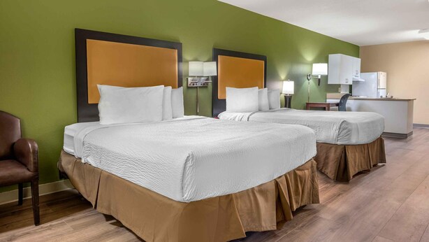 Habitación de hotel con dos camas, un escritorio, una silla y un kitchenette.