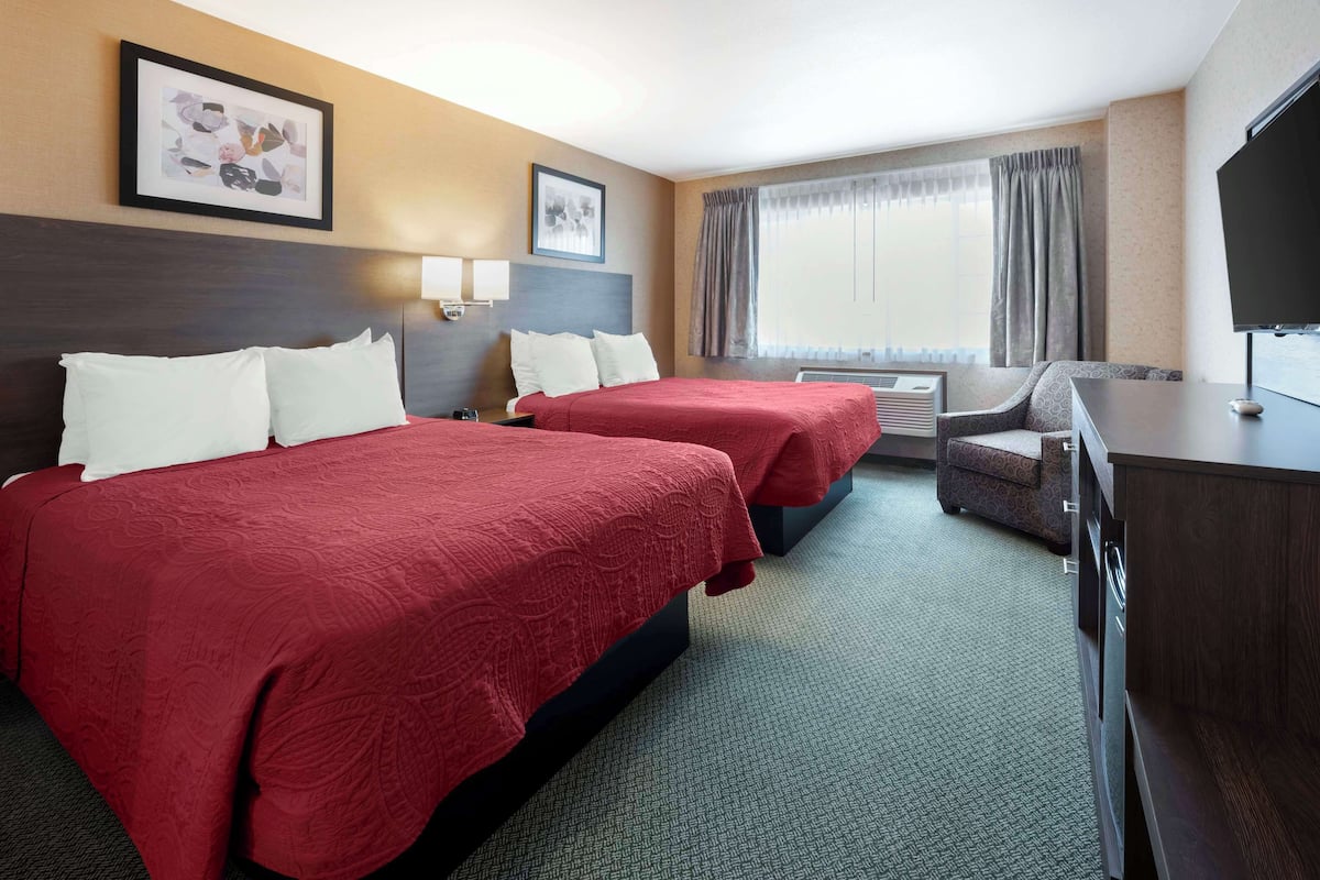 A hotel room with two beds, a desk, a TV, and a window with curtains.