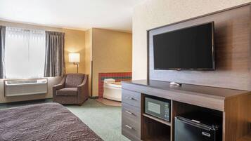 Ein Hotelzimmer mit Bett, Fernseher, kleinem Kühlschrank, Sessel, Toilette und Klimaanlage.