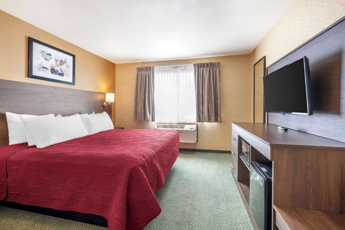 A hotel room with a large bed, a flat-screen TV, a desk with a computer, and a window with curtains.