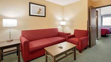 Una habitación de hotel con un sofá rojo, una mesa de centro de madera, una lámpara y un cuadro en la pared.