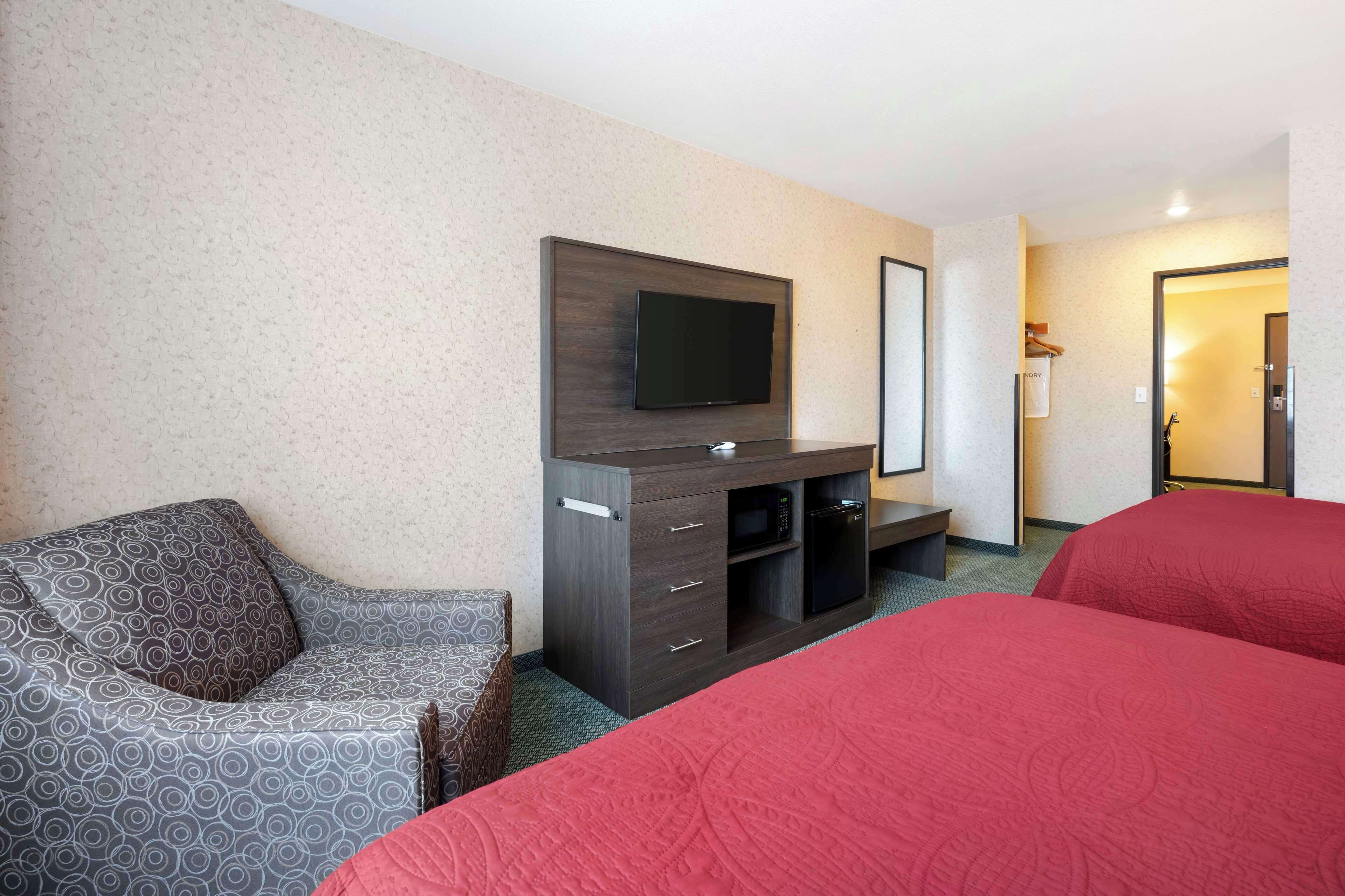 Habitación de hotel con un sofá, un televisor montado en un mueble de madera y dos camas con ropa de cama roja.