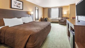 Een hotelkamer met een groot bed, een bureau, een stoel, een televisie en een raam met gordijnen.
