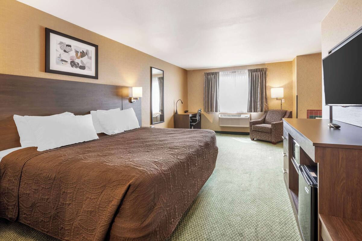 A hotel room with a large bed, a desk, a chair, a TV, and a window with curtains.