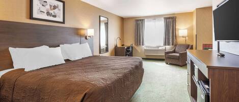 A hotel room with a large bed, a desk, a chair, a TV, and a window with curtains.