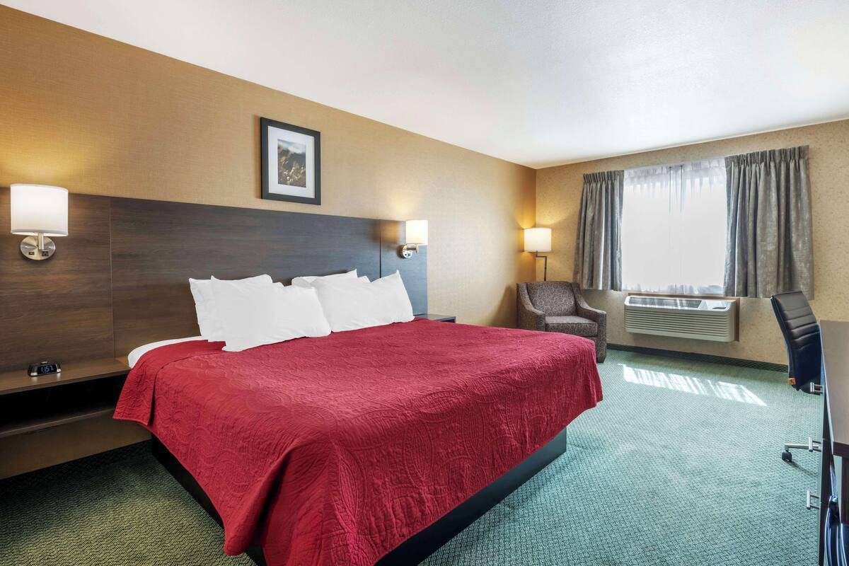 A hotel room with a large bed, two bedside lamps, a chair, a desk, and a window with curtains.
