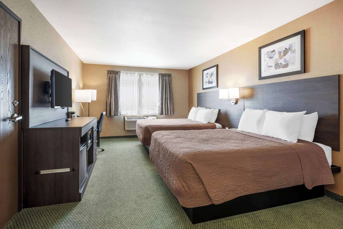 A hotel room with two beds, a desk, a television, and a window with curtains.