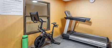 Un gimnasio con una bicicleta estática, una cinta de correr y una botella de agua verde.