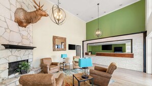 A spacious living room with a stone fireplace, mounted deer head, and modern furniture. - Best Western George West Executive Inn (George West)