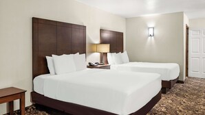 A hotel room with two beds, a bedside table, a lamp, and a door. - Best Western George West Executive Inn (George West)