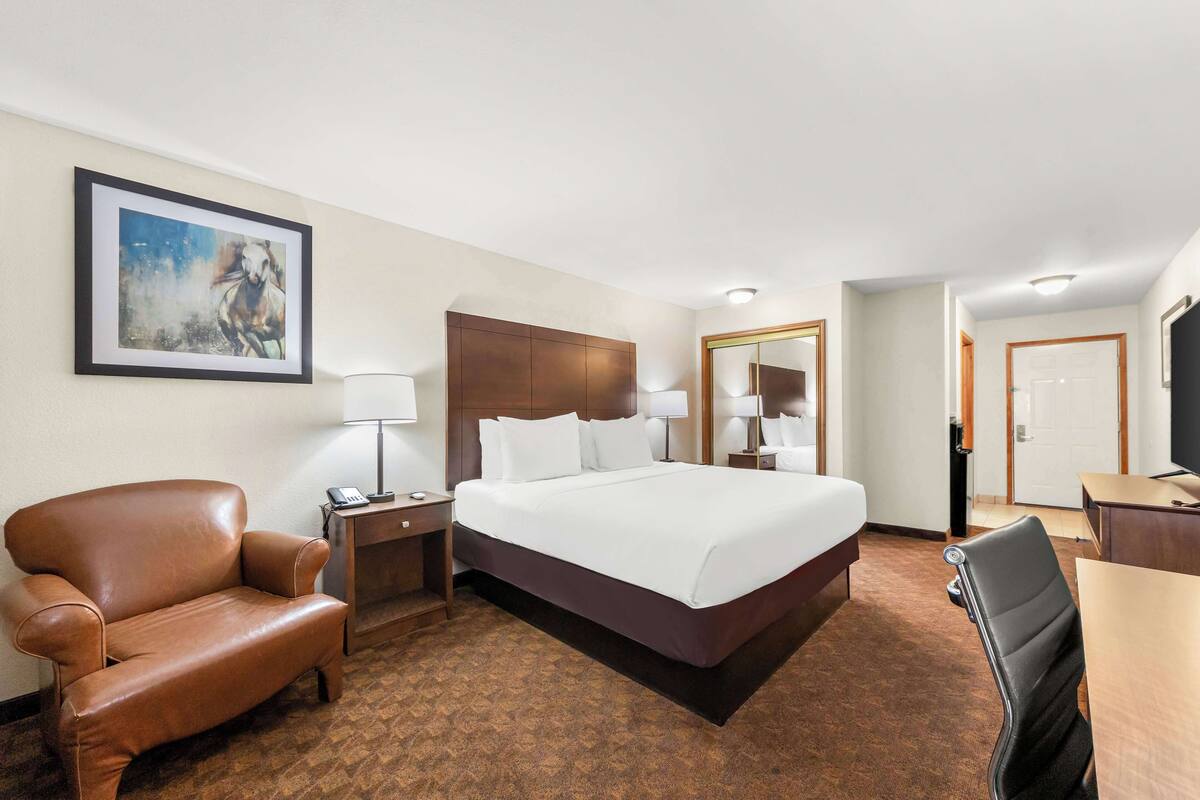 A hotel room with a large bed, a brown leather chair, a desk, and a painting on the wall.