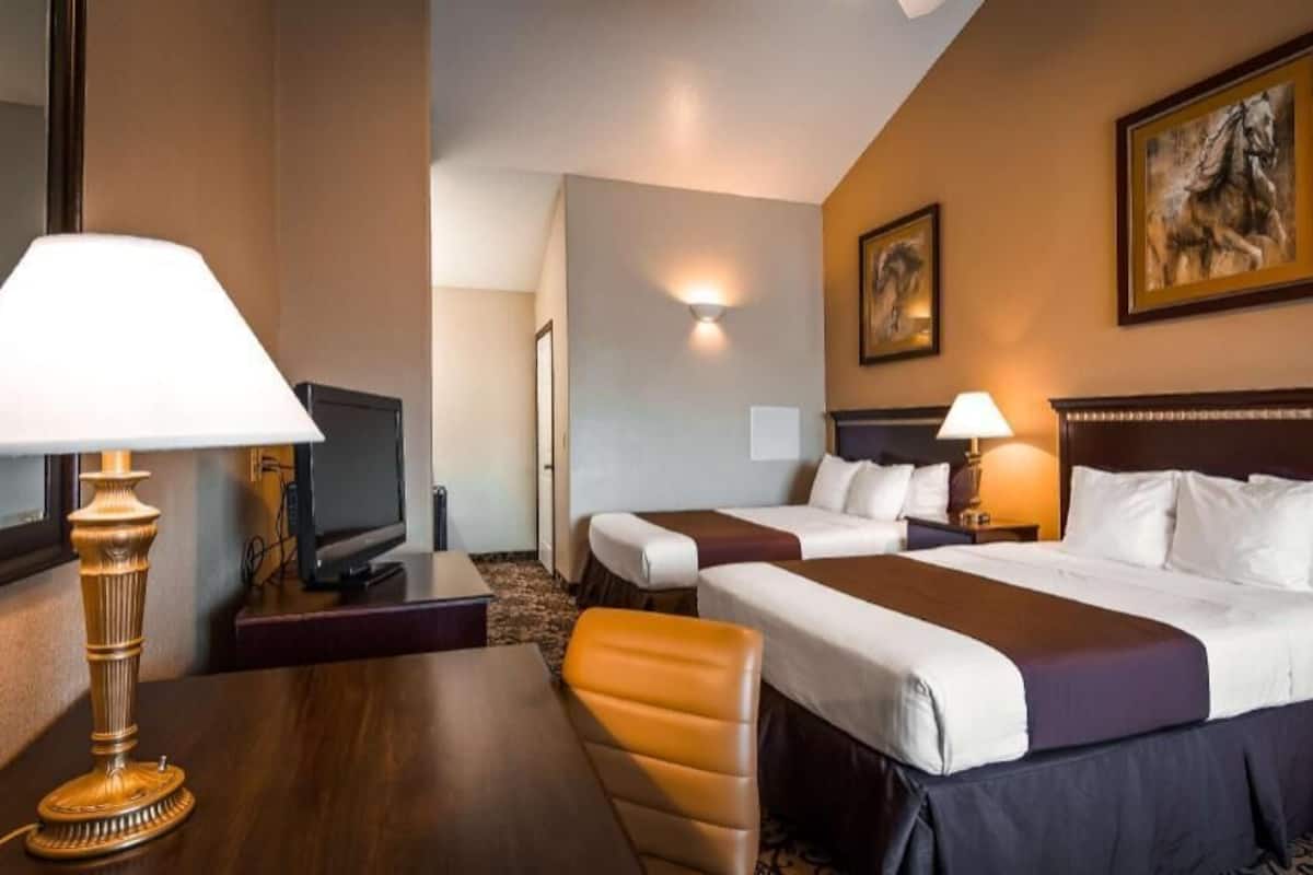 A hotel room with two beds, a desk, a chair, a TV, and artwork on the walls.