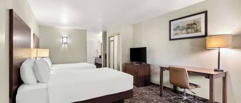 Quarto de hotel com uma cama grande, uma mesa com cadeira, televisão e carpete estampado.